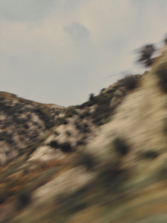 A blurry, motion-streaked view of a rocky desert hillside under an overcast sky, suggesting high speed.