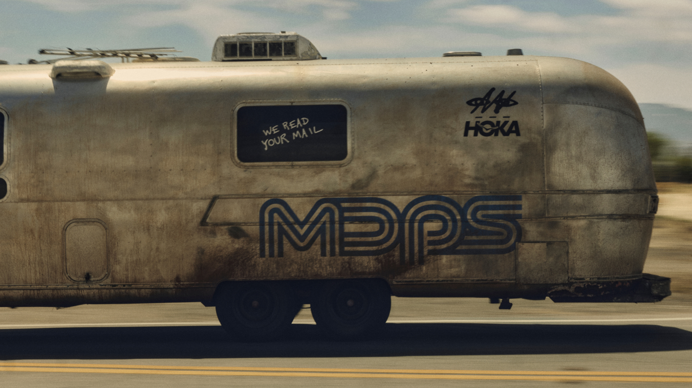 A profile view of the weathered silver trailer showing the blue "MDPS" graphic and a window with the handwritten text "WE READ YOUR MAIL."