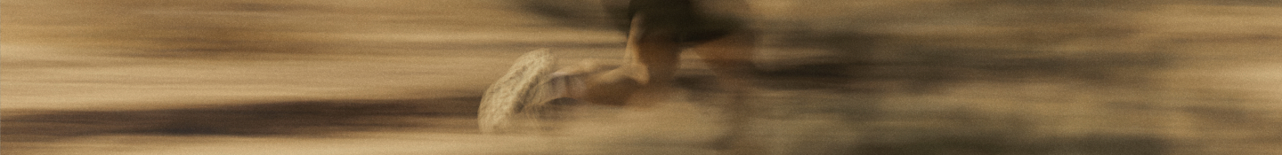 A long, panoramic, and highly blurred motion shot of a runner's feet kicking up dust on a desert trail.