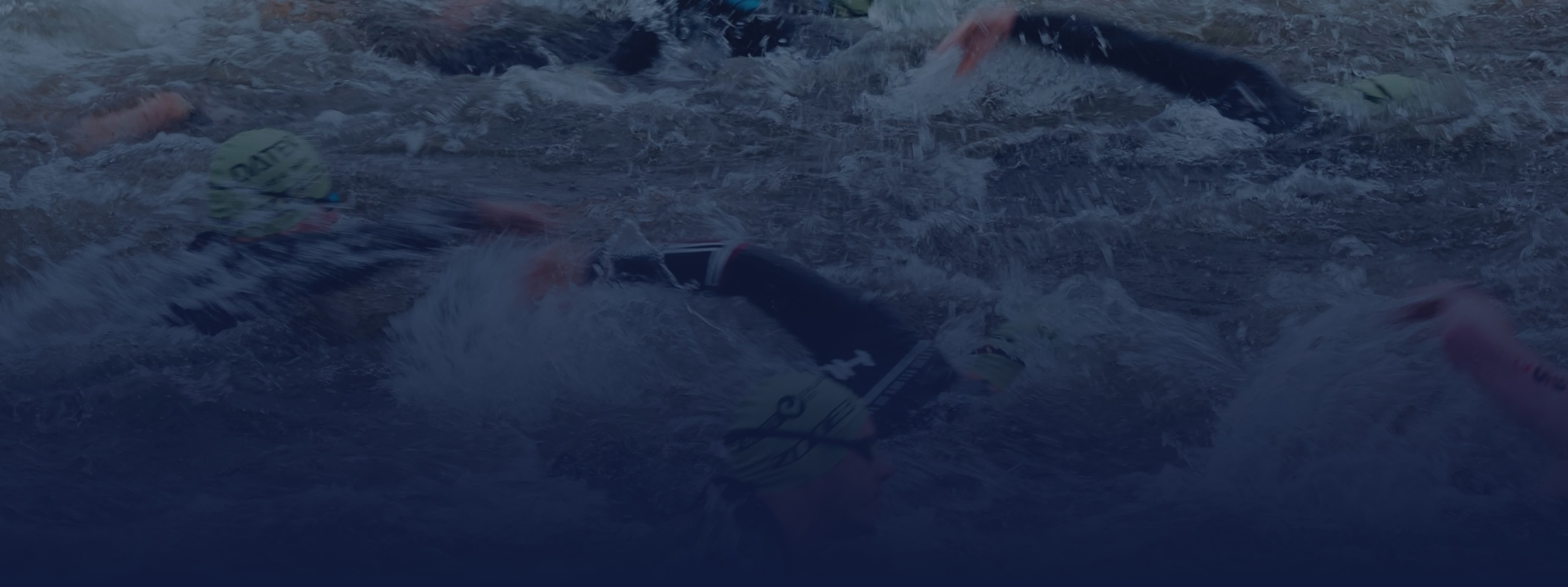 Multiple swimmers in wetsuits and caps in dark, choppy water with splashes.