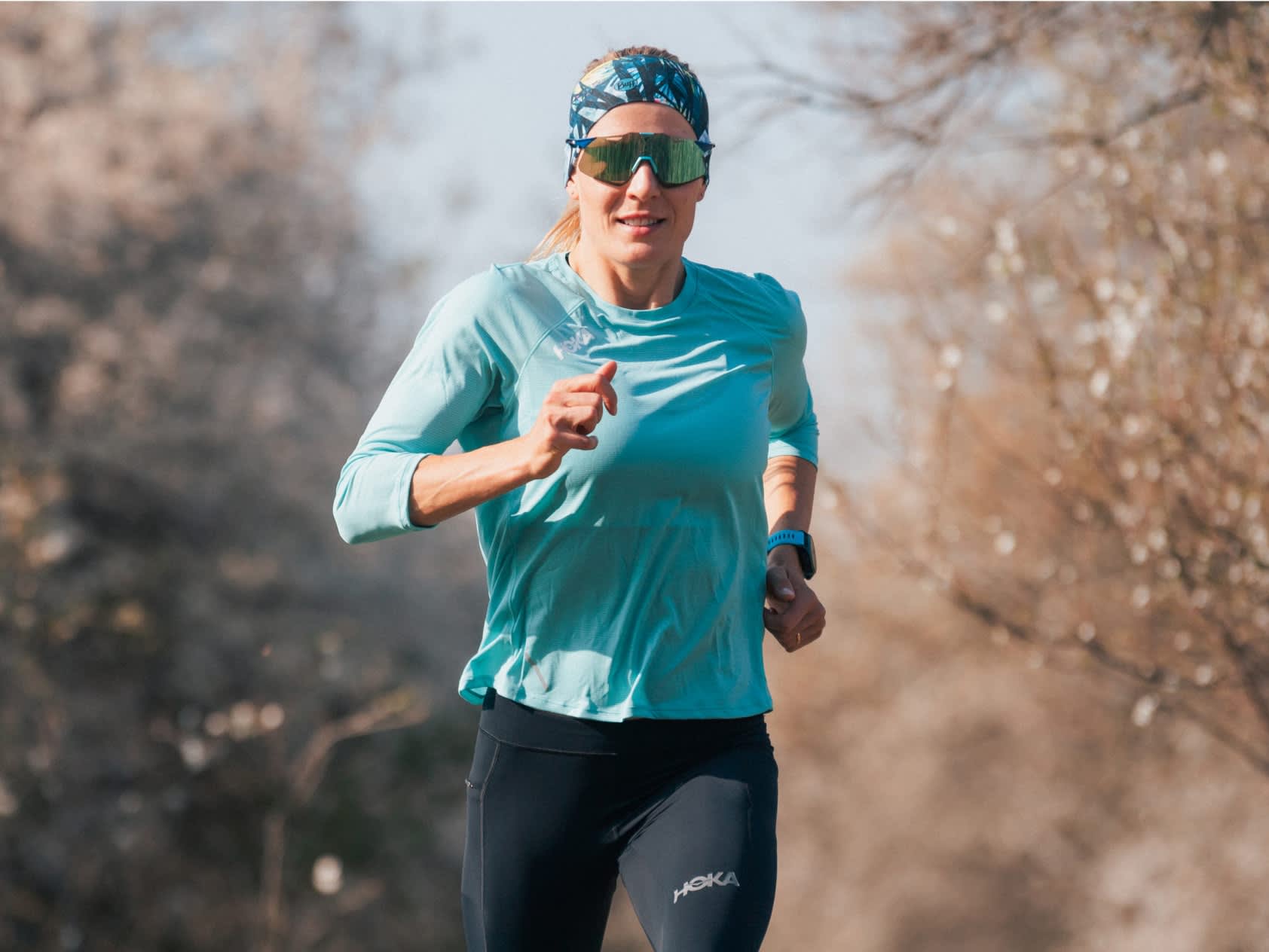 Person running outdoors, wearing teal top, black leggings, patterned headband,