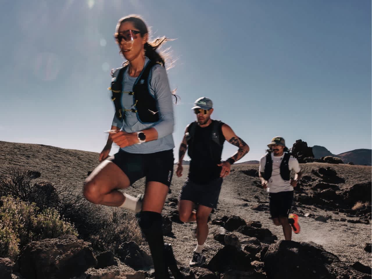 Three trail runners moving across a rocky desert landscape.