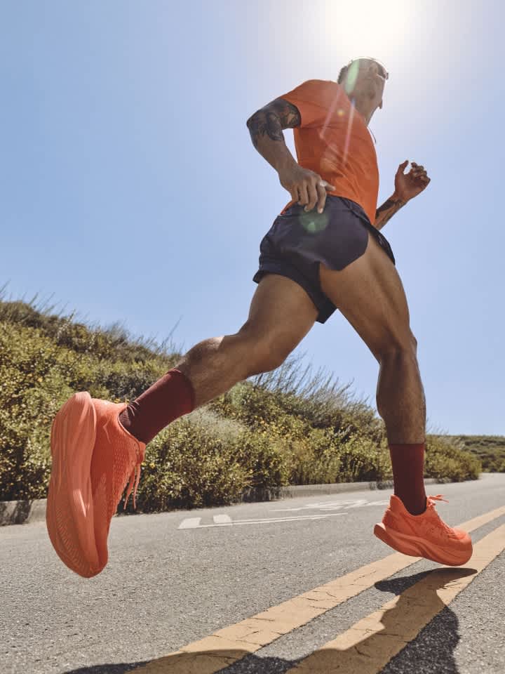Low angle of runner in orange top and shorts with orange shoes on sunny road.