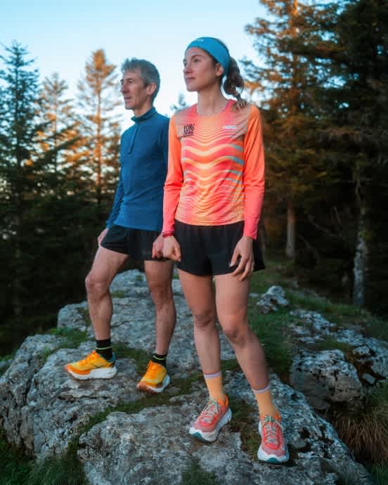 Two runners in colorful athletic wear and trail shoes standing on rocks.
