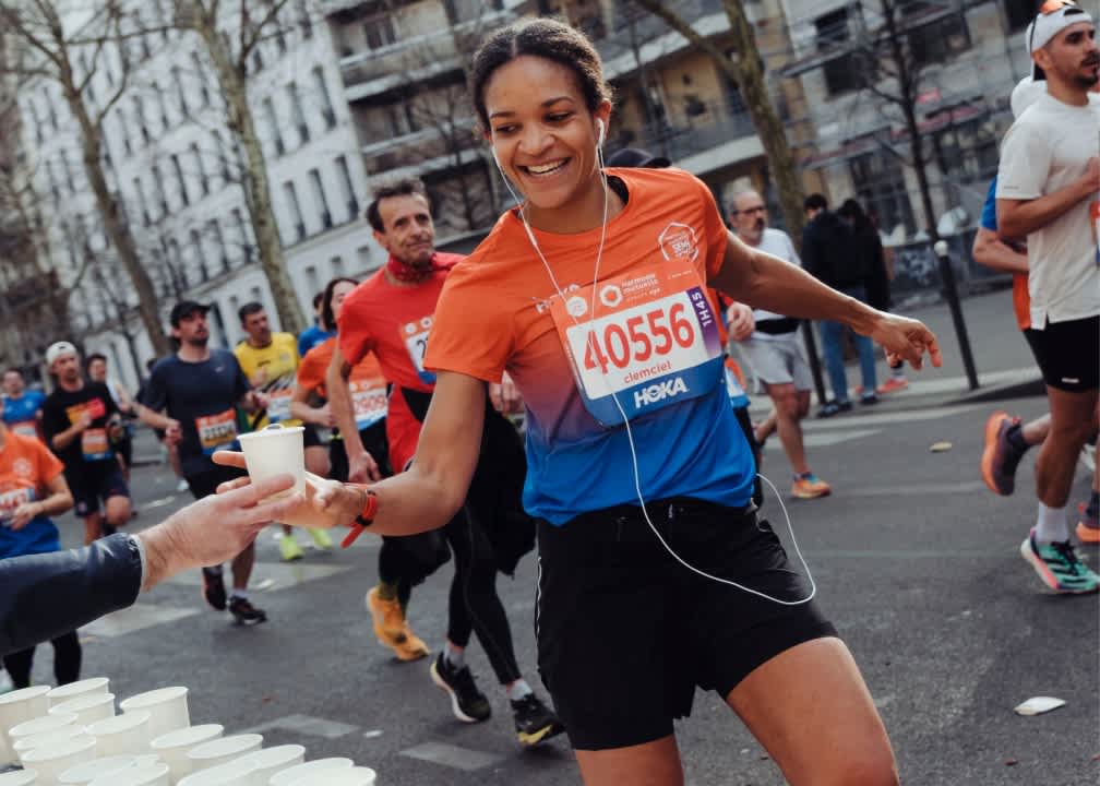 Smiling runner with bib 40556 taking water from volunteer at race aid station.