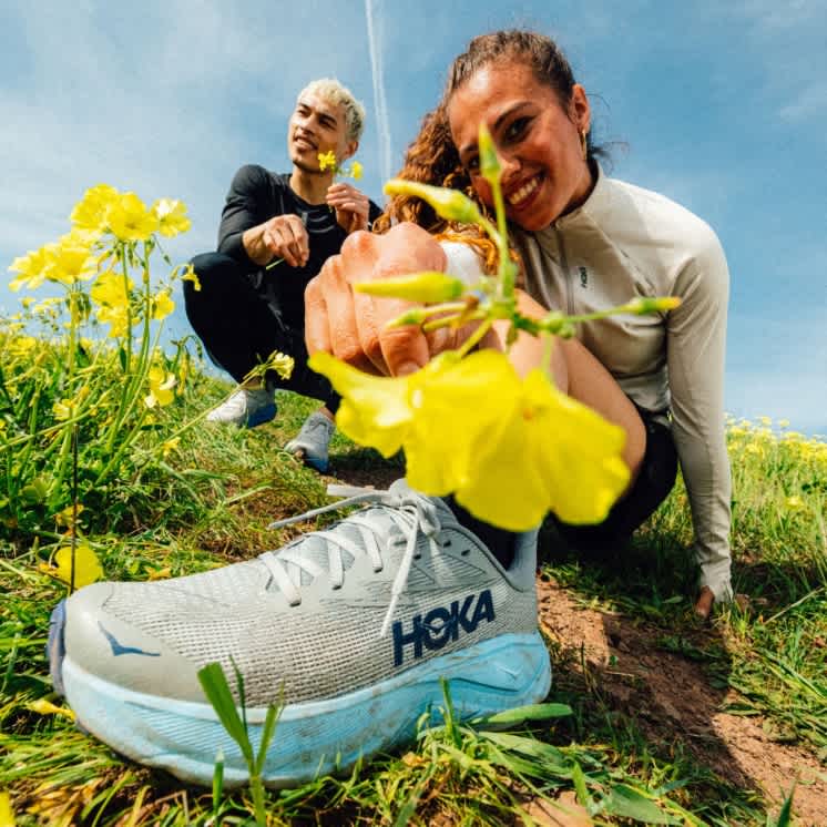 Models pose in HOKA trainers in a sunny field of flowers.