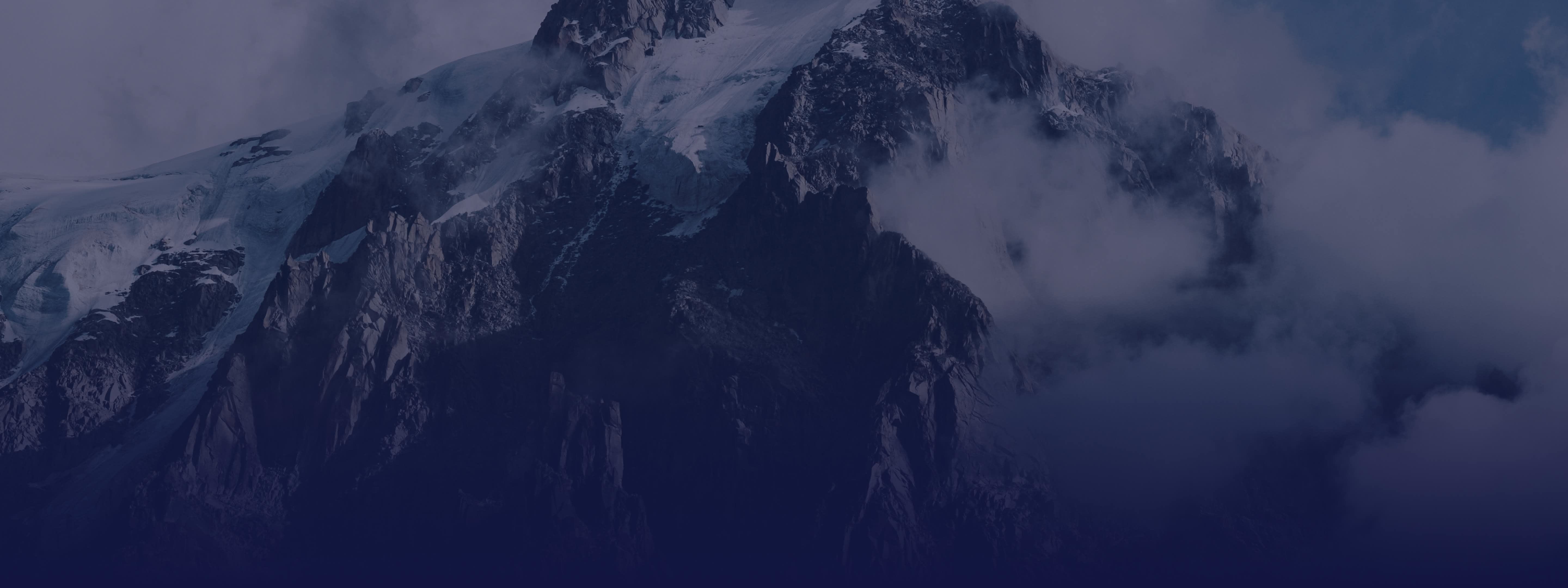 Panoramic view of dark, snow-capped mountains and glaciers shrouded in mist.