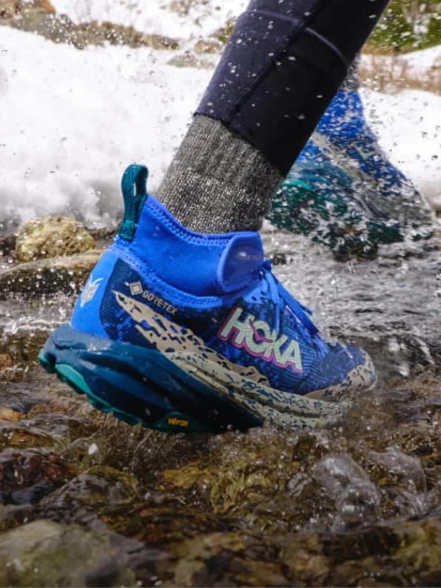 Close-up of person in blue Hoka GORE-TEX shoe splashing water in a rocky stream.