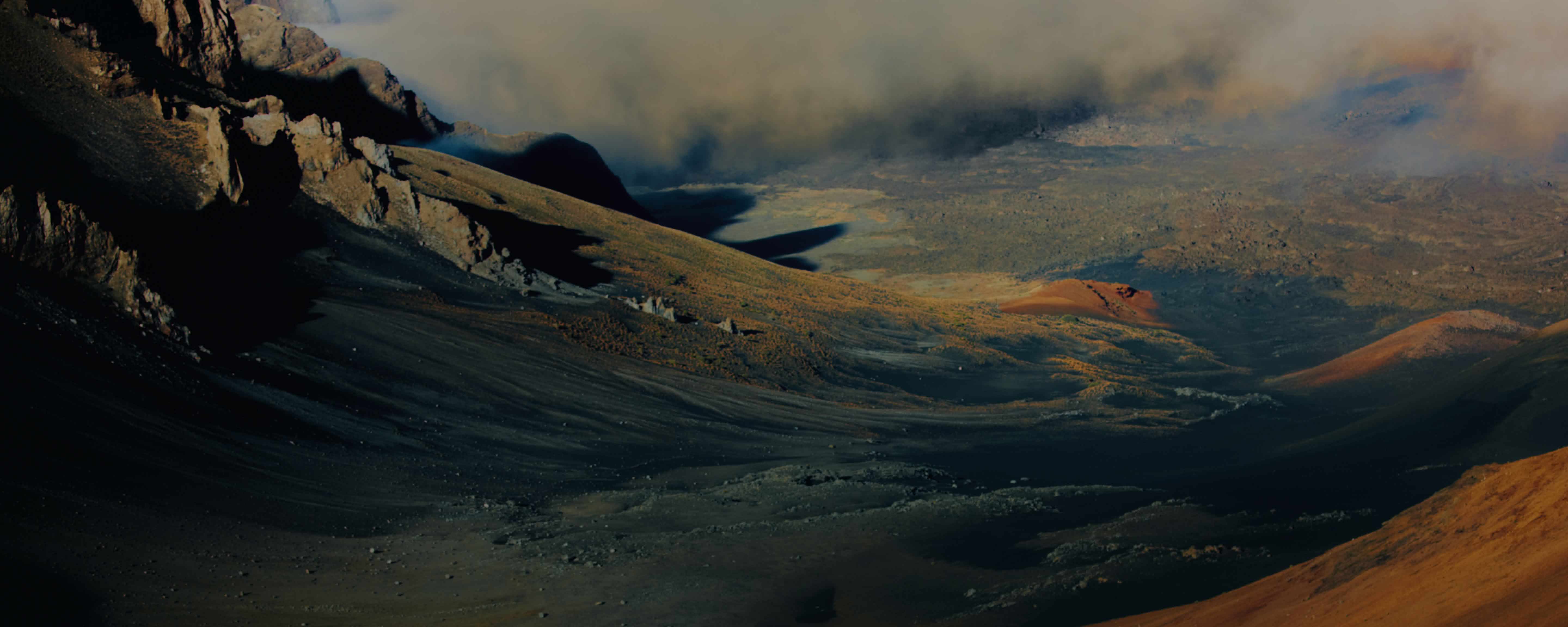 Panoramic view of a volcanic caldera with dramatic light and sweeping clouds.