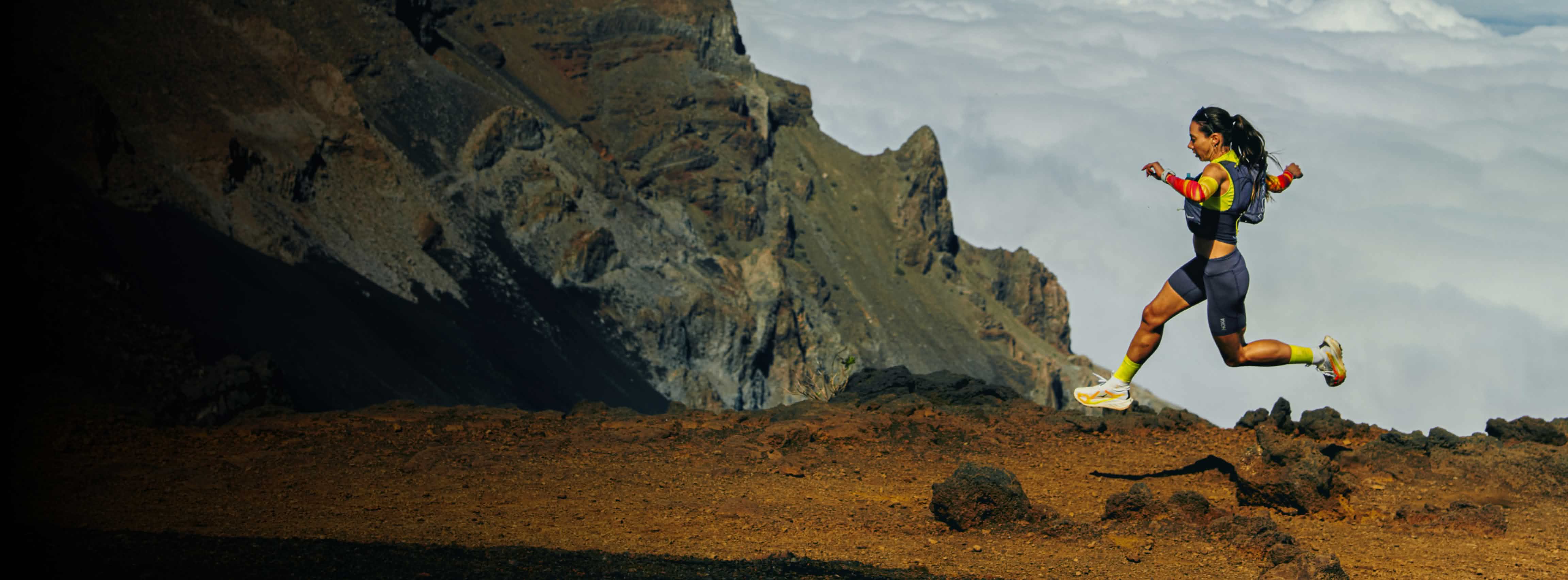 Athlete running on rocky mountain trail with clouds. Quote about HOKA Tecton X 4