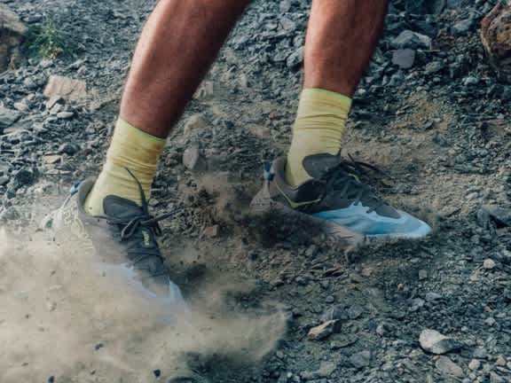 Close up of a runner kicking up dust as they traverse a gravelled hillscape