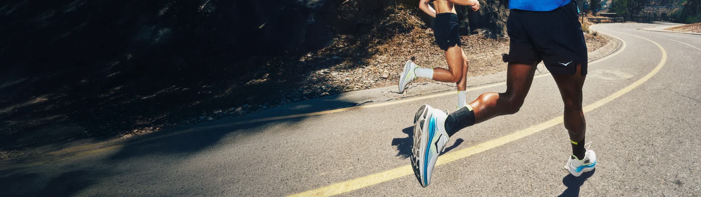 Two runners on an asphalt road with a yellow line, showcasing athletic footwear.