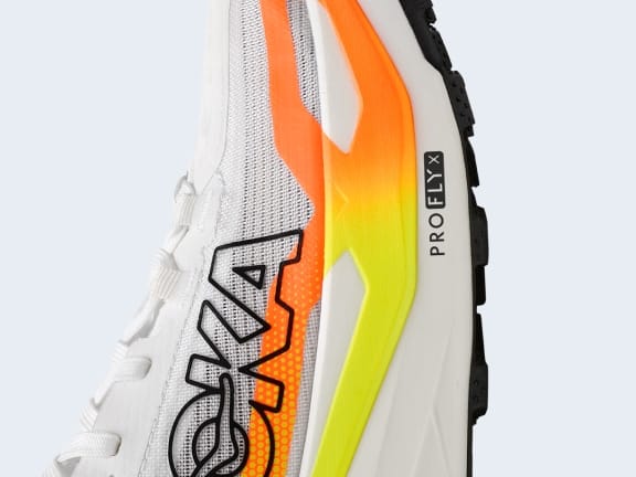 White mesh HOKA running shoe with orange-yellow gradient midsole, "PROFLY™
                                        X".
