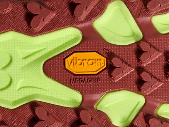 Close-up of a shoe sole: red, lime green, with orange Vibram® Megagrip logo.