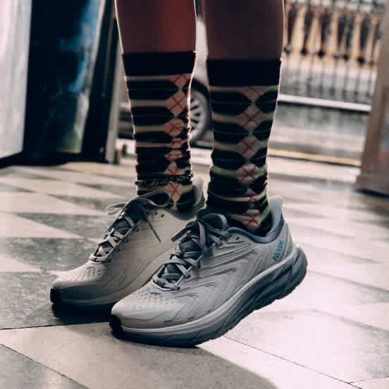 Close-up of person wearing patterned socks and light grey Hoka running shoes.