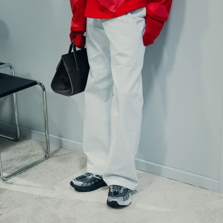 Person in red top, white wide-leg pants, grey sneakers, holding a dark handbag.