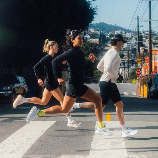 Three runners on a crosswalk in a city street with houses on hilly background.