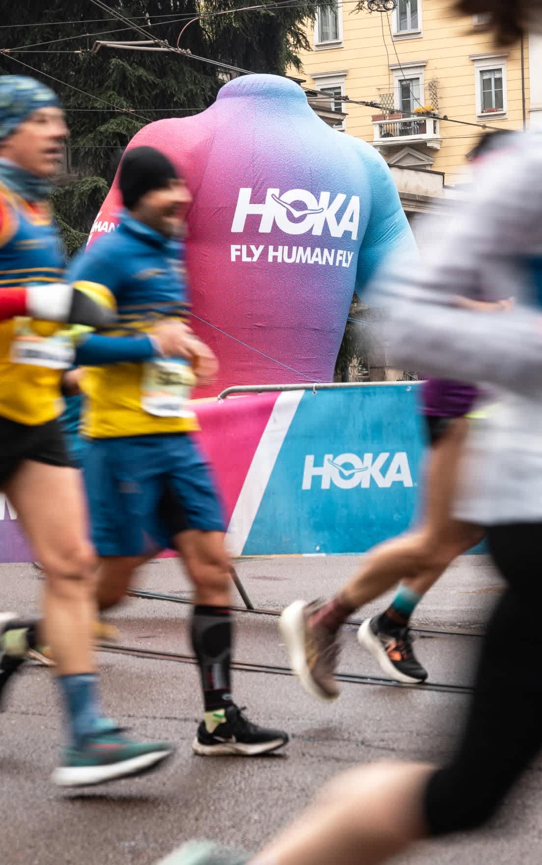 Blurred runners pass a large gradient HOKA inflatable mascot at a race event.