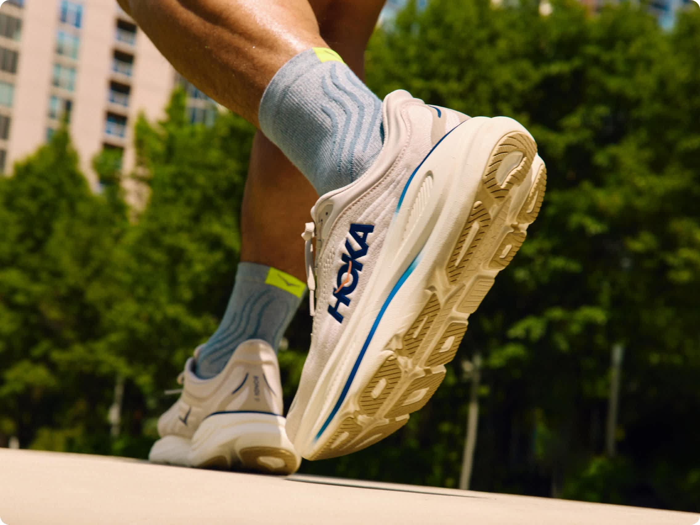 Close-up of a person's legs, HOKA running shoes, and blue socks while stepping