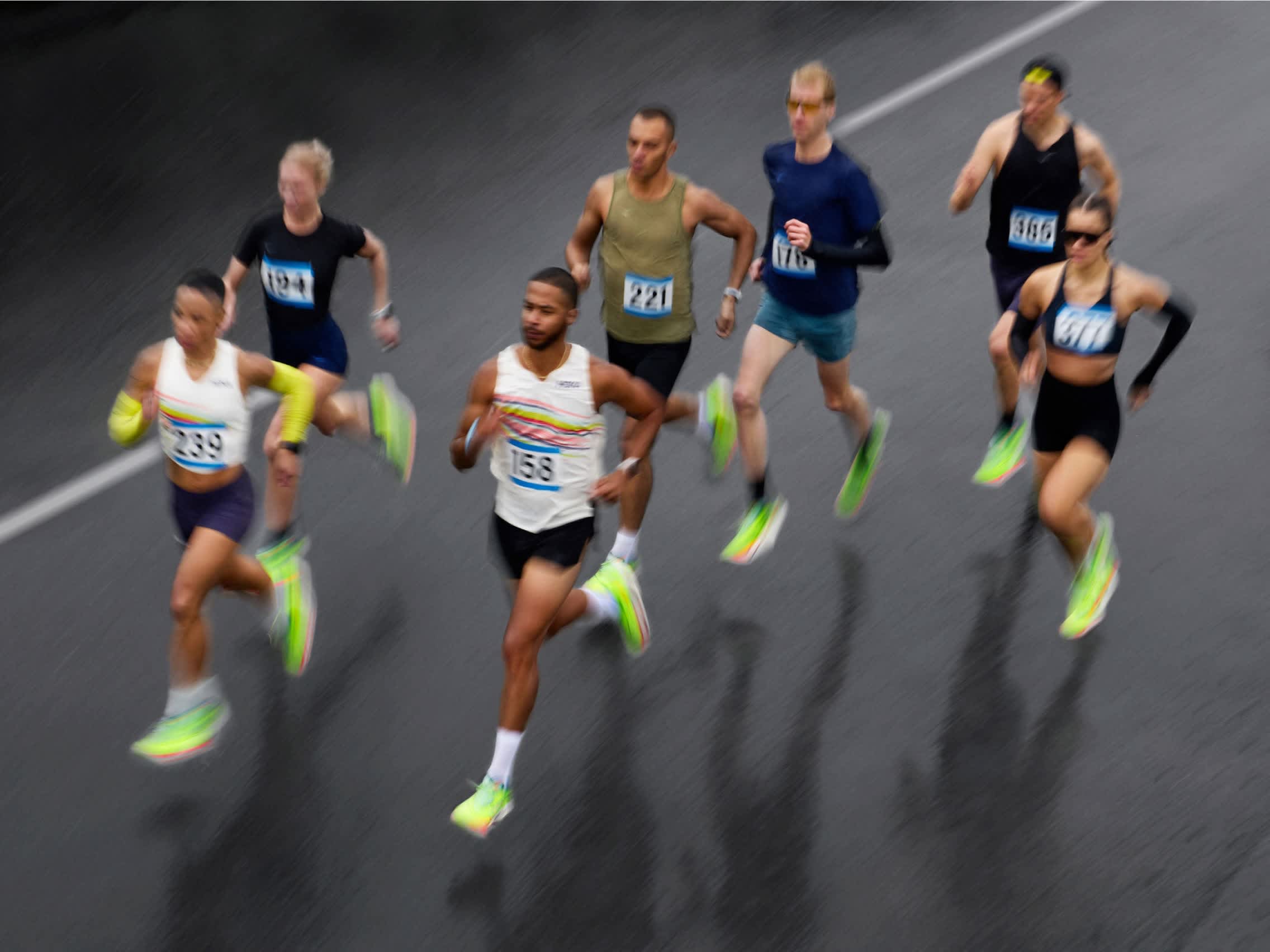 Multiple runners with motion blur on a wet road during a race.