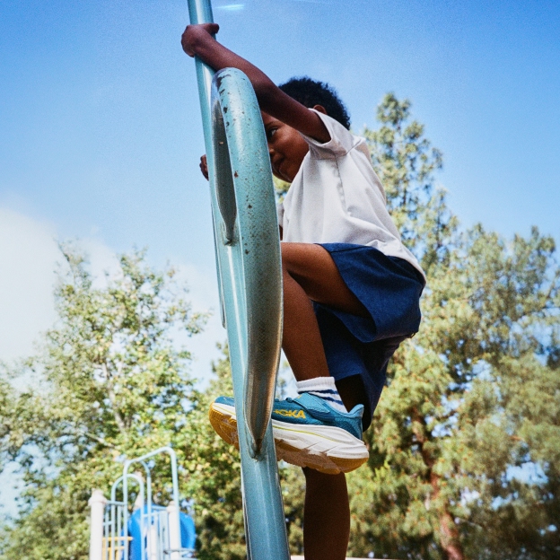Little child climbing on a climbing frame, wearing HOKA's on a sunny day 
