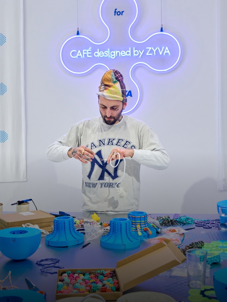 Individual crafting with colorful materials, blue objects, under a neon 'ZYVA' sign.