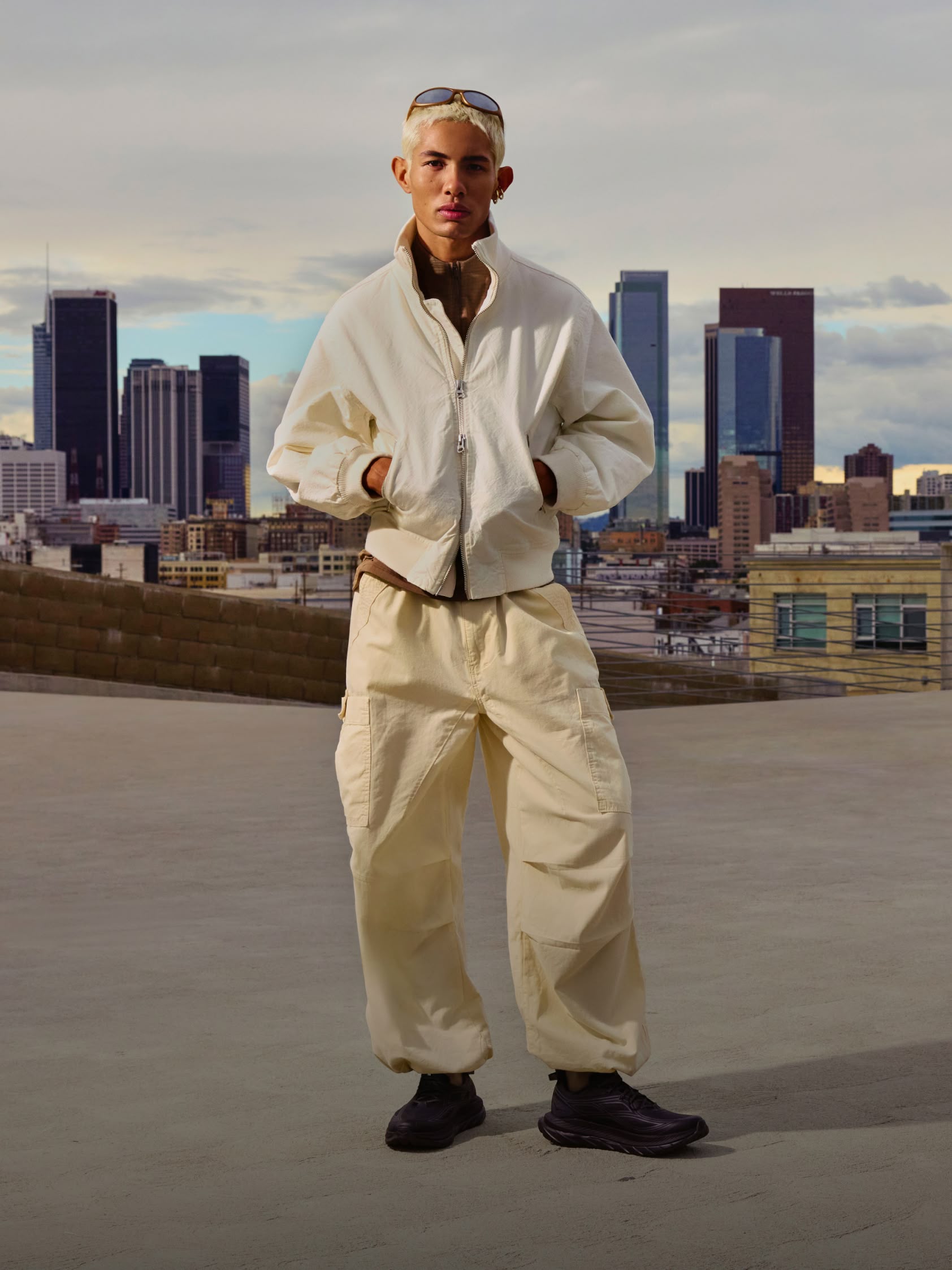 A male model poses against a city skyline in HOKA Mach Remastered trainers.