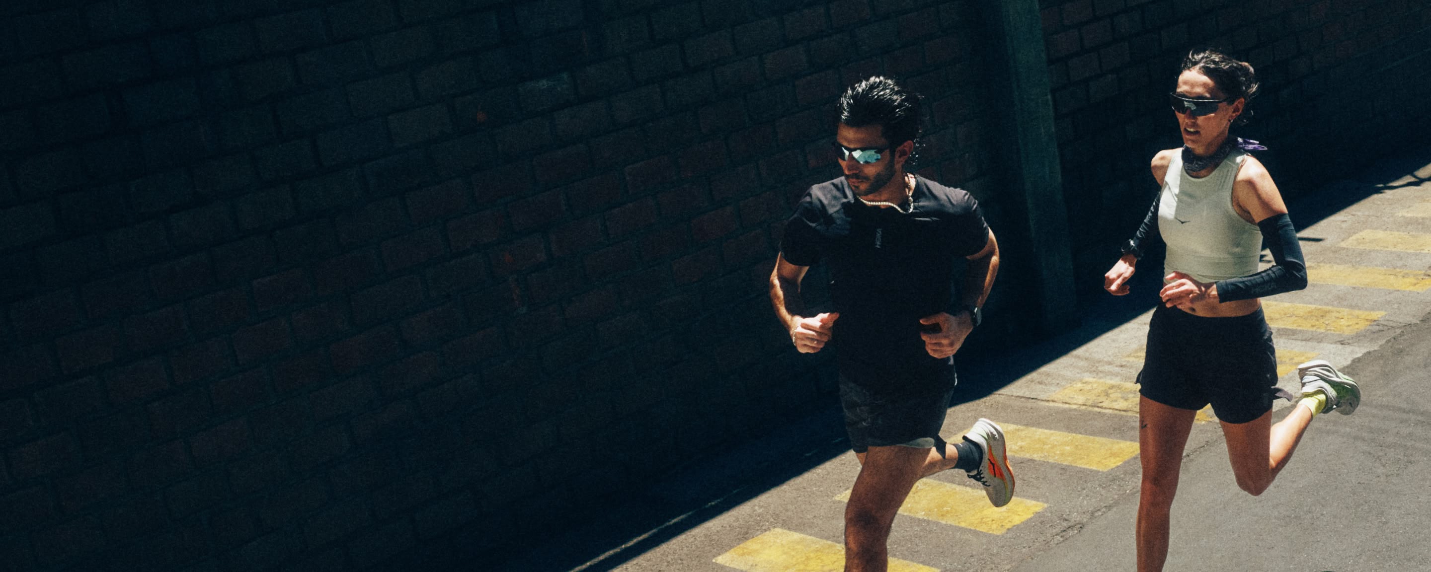 Two runners run across a city road in HOKA kit.