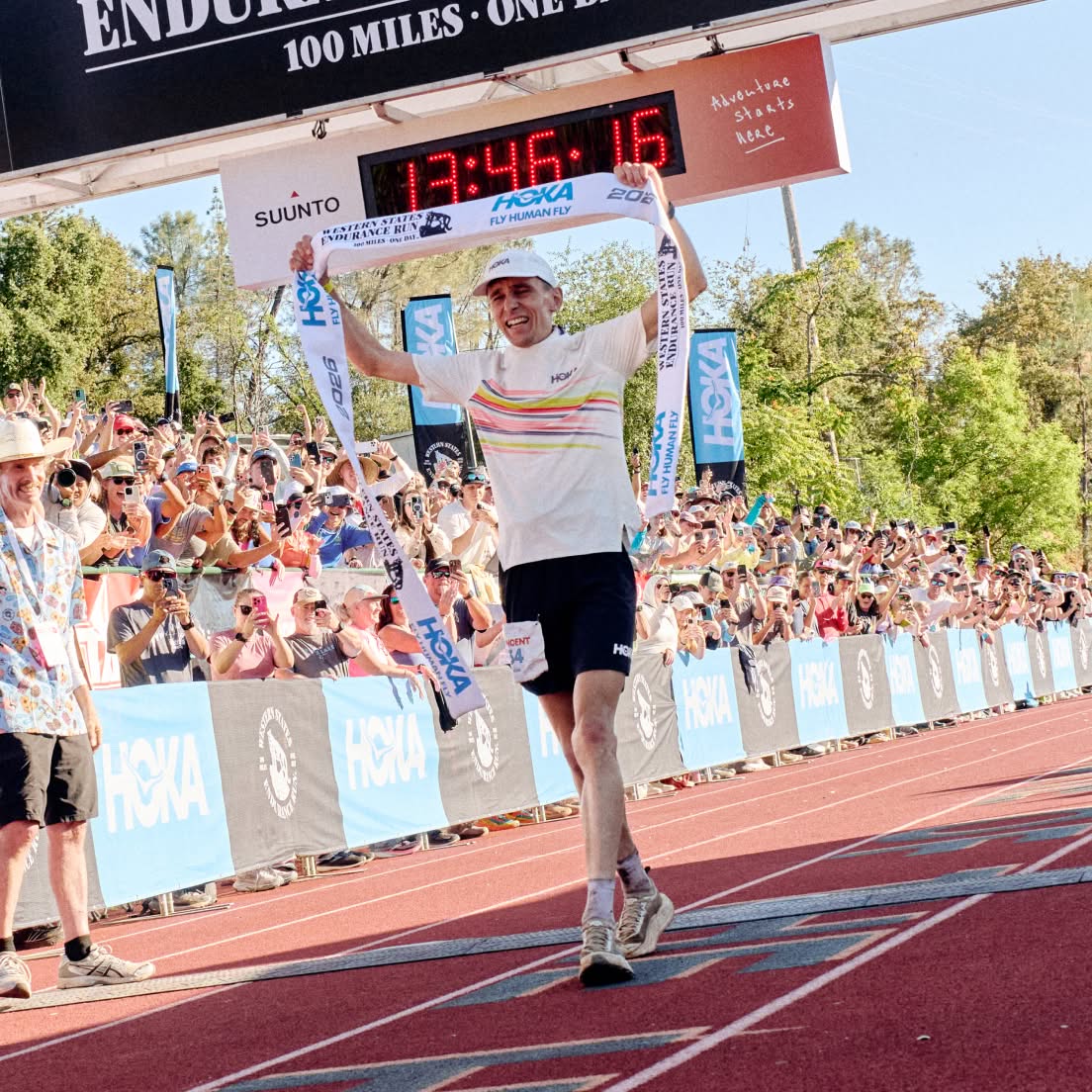 Runner at finish line, celebrating with HOKA banner. Clock shows 13:46:16 and a crowd.
