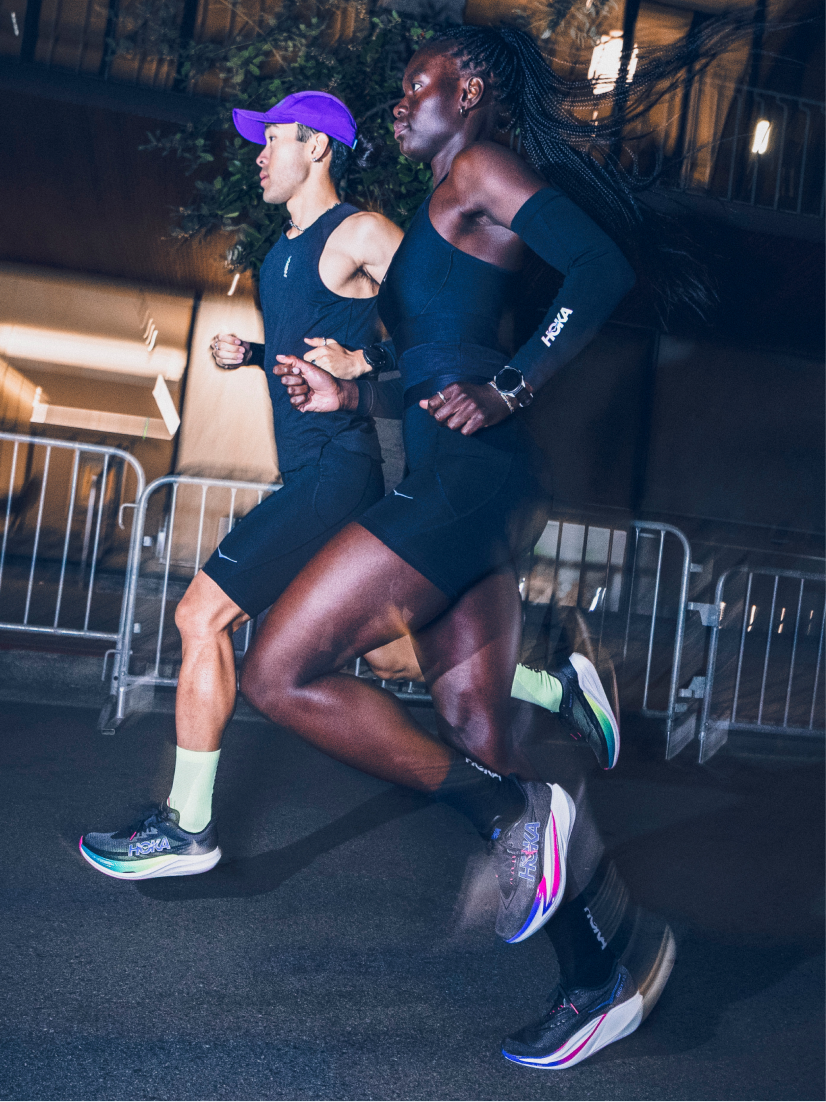 Sweaty athlete drinks from blue bottle; another athlete watches, against ribbed wall.
