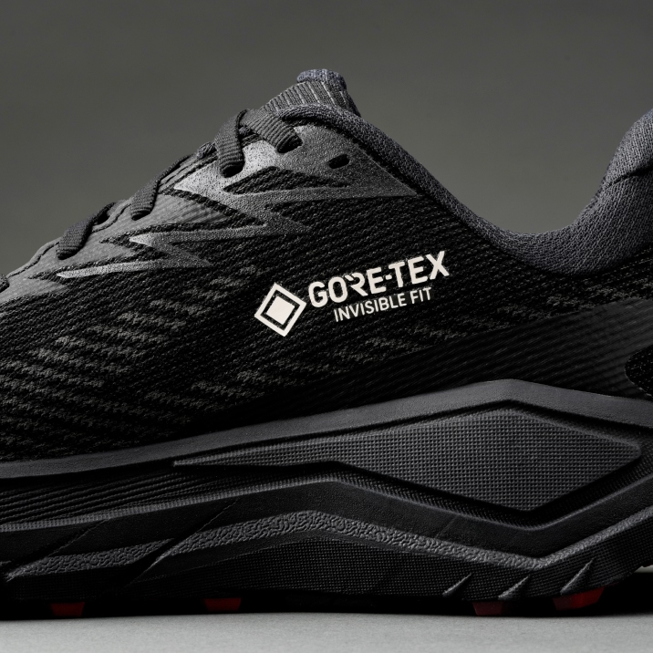 Four Hoka running shoes on asphalt; dark uppers and vibrant gradient soles.