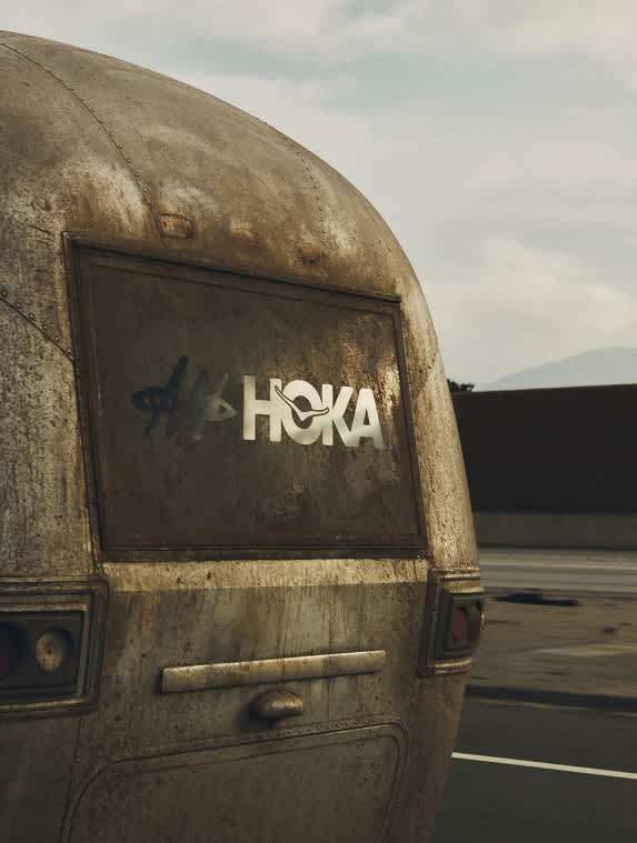 The rounded, weathered rear of a vintage metal trailer viewed from behind, featuring a silver HOKA logo in a window.