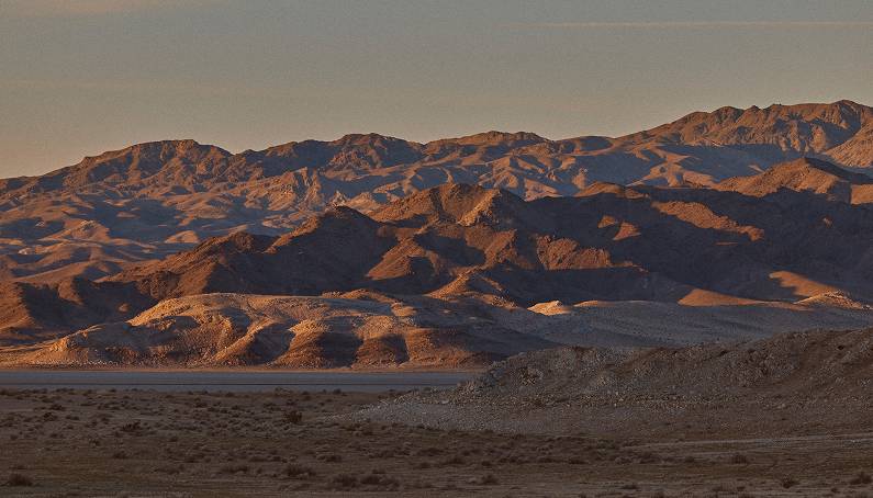 A scenic view of rugged, layered desert mountains illuminated by the warm, golden light of sunset.
