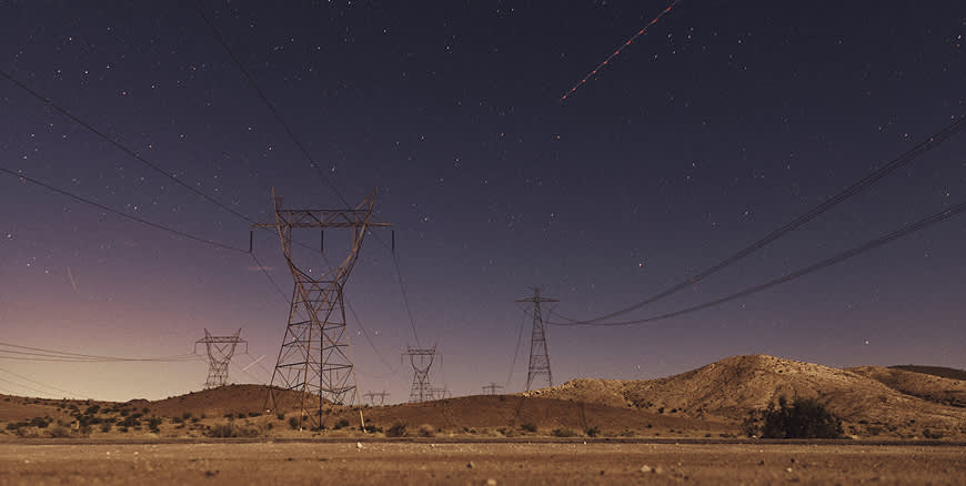 A wide night shot of a desert landscape featuring silhouettes of power lines under a vast, starry sky.