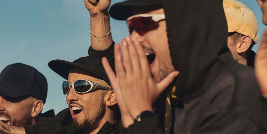 A close-up of a group of people wearing sunglasses and hats, cheering and shouting with excitement.