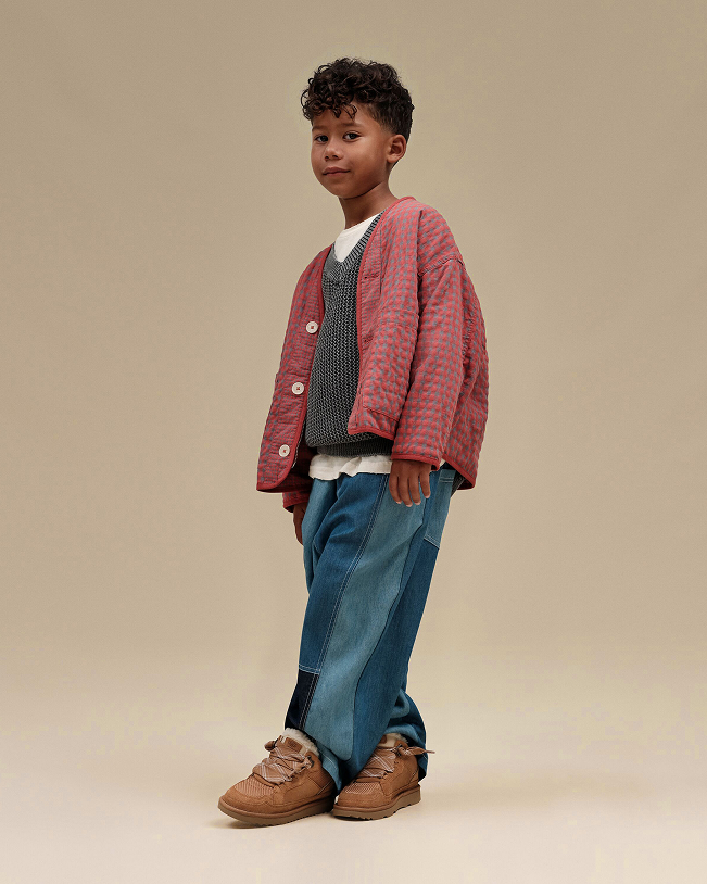 Child in red cardigan, grey vest, white shirt, patchwork jeans and brown shoes.