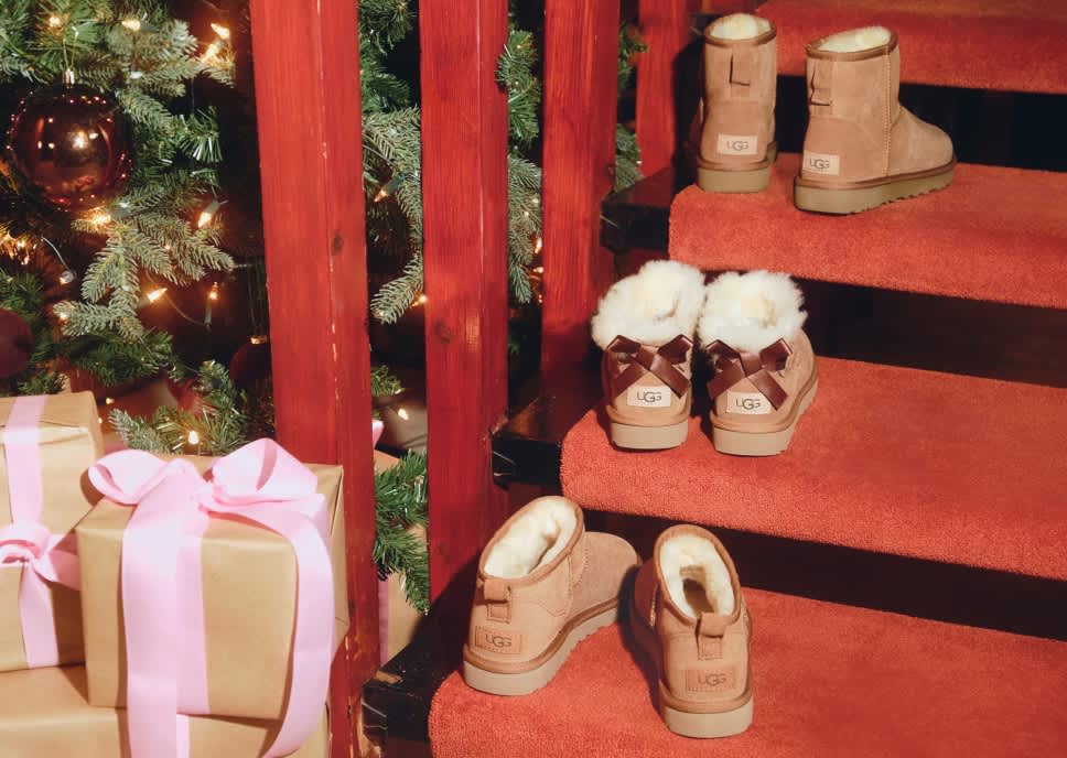 Ugg boots on red stairs next to a Christmas tree and gift boxes.