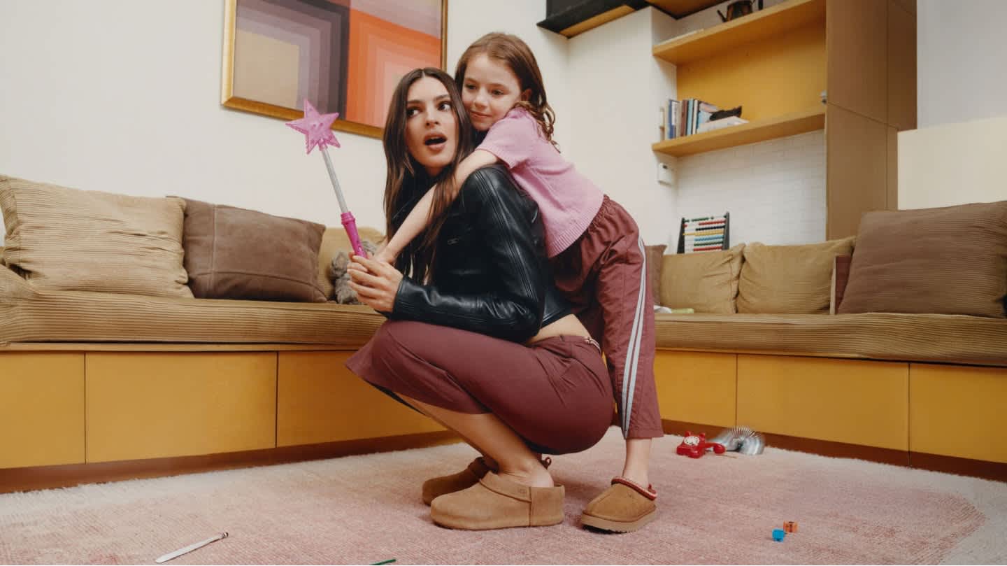 Adult squats holding wand, child hugs from behind, both in slippers on toy-strewn