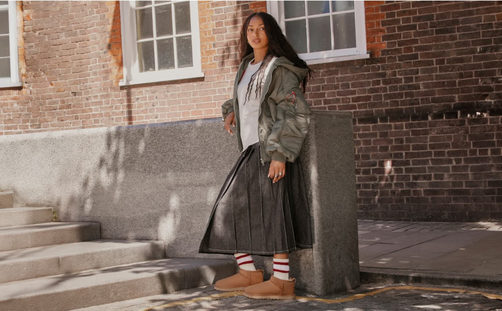 UGG boots styled with striped socks, midi skirt and bomber jacket outside.