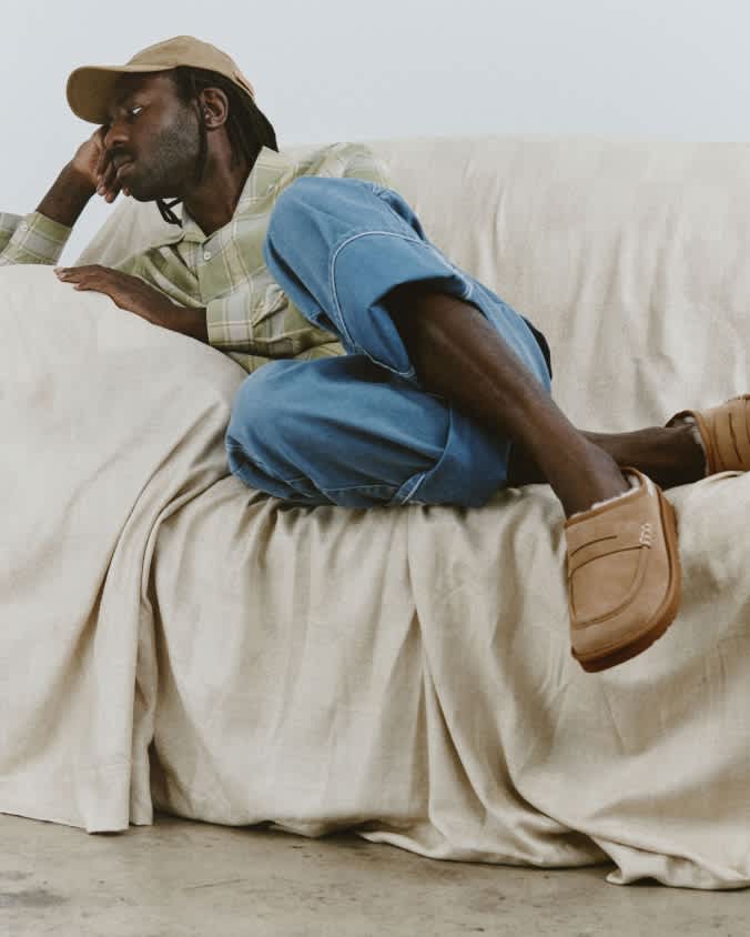 UGG JW Anderson loafers styled with cuffed denim trousers on a draped sofa.