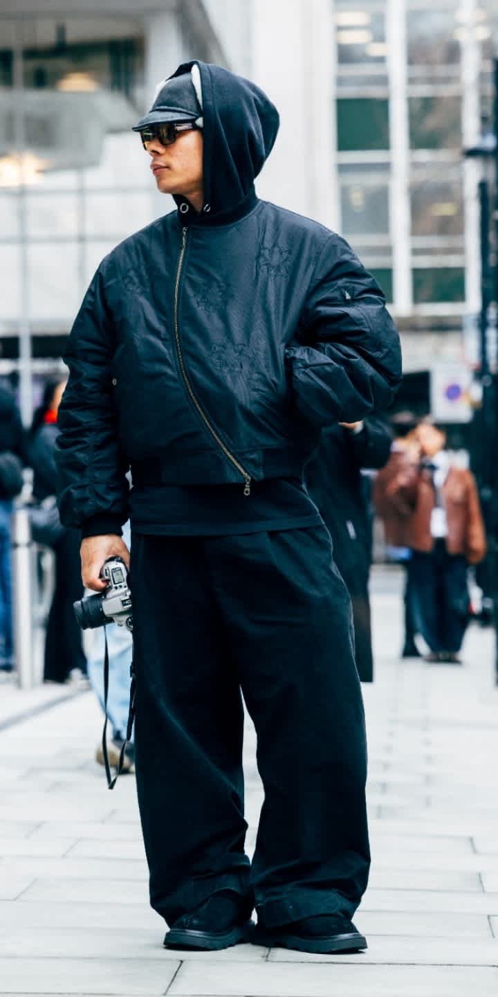 A person wearing a black hooded jacket, black baggy jeans and the Tasman Lug in Black, standing in the street. 