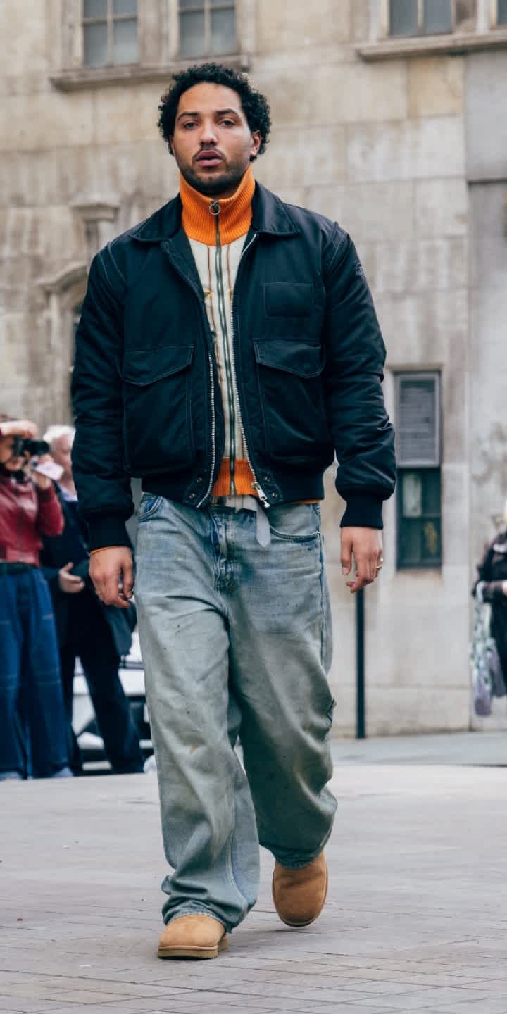 A person wearing blue baggy jeans, a black jacket and the Classic Ultra Mini in Chestnut, walking in a street.