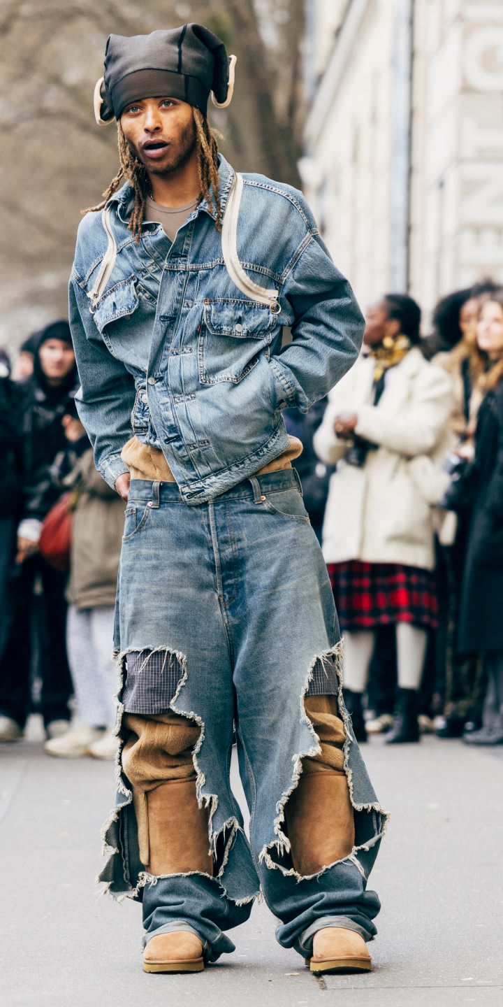 A person in a distressed denim co-ord and black hat, worn with the Classic Tall Boot, standing in front of a crowd.