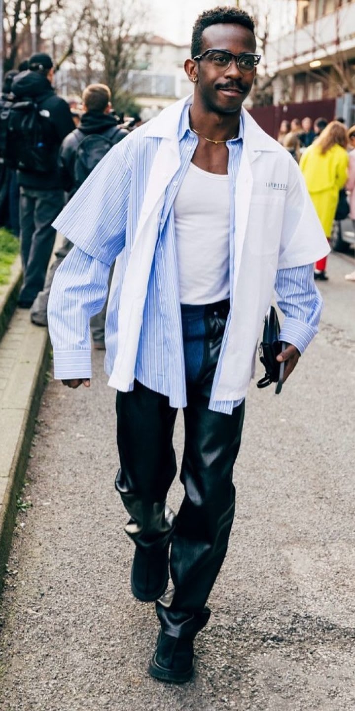 A person in a blue layered shirt and leather pants, worn with the Tasman Lug, walking in front of a crowd.