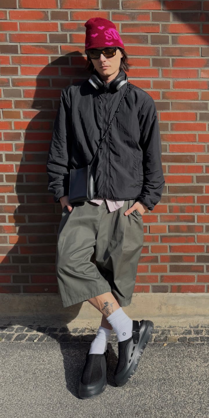 A person wearing khaki green 3/4 length shorts, a black jacket, a red hat and the PeakMod in Black with white socks. 