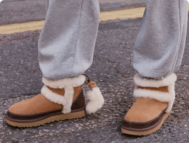 Person in grey sweatpants wearing tan UGG-style boots with cream trim & a charm.