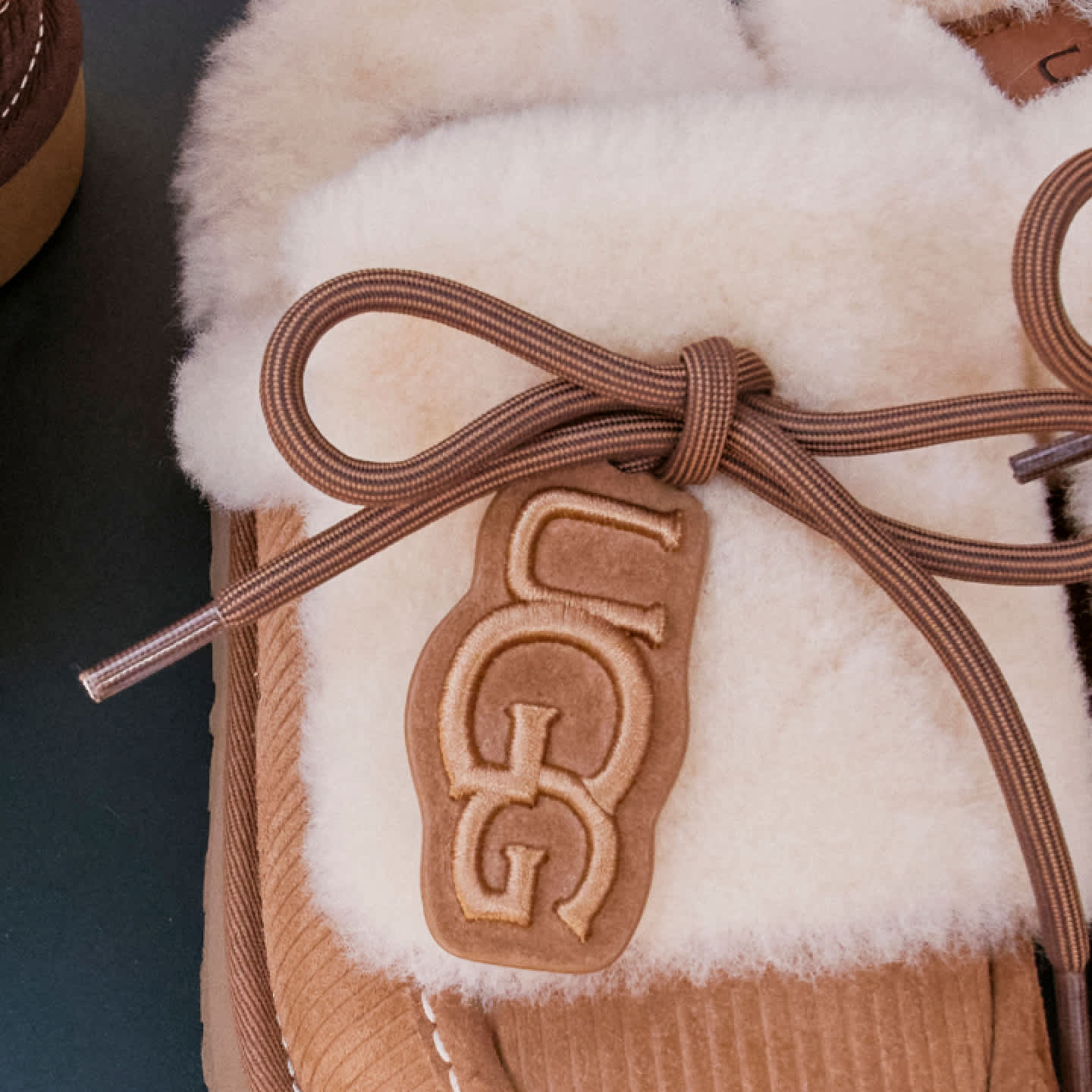Close-up of a UGG Heritage Lace-Up Slipper with logo tag and laces.