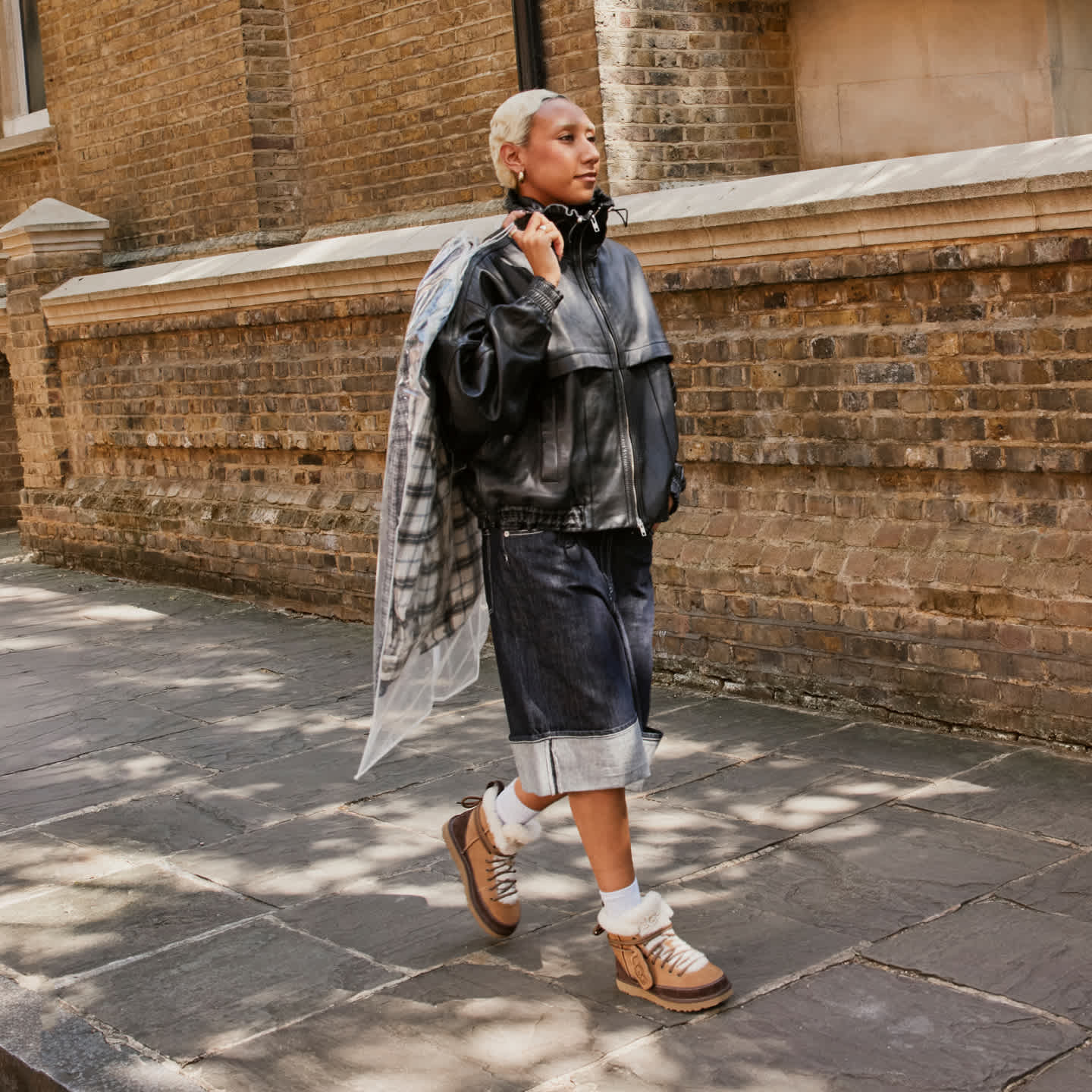 Person in black jacket, denim shorts, and Classic Heritage Lace-Up Boots walks.