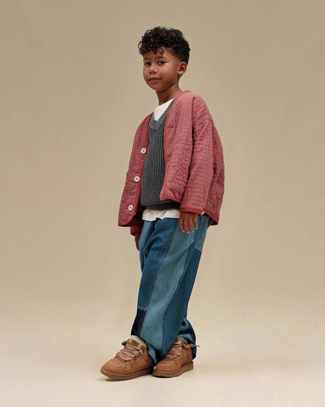 Model standing in a patterned cardigan, patchwork jeans and suede clogs.