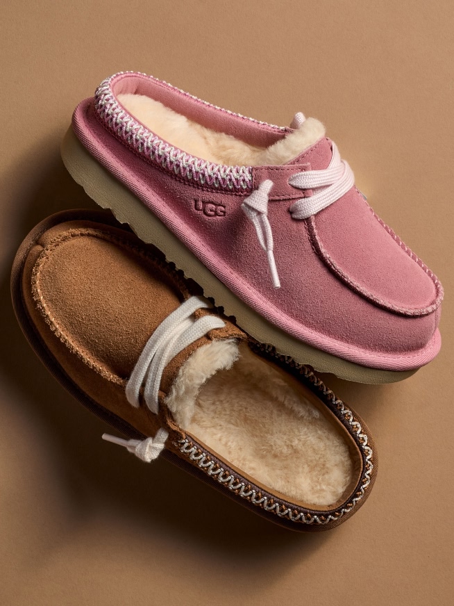 Two UGG slippers, one pink, one tan, with white laces and fluffy interiors.